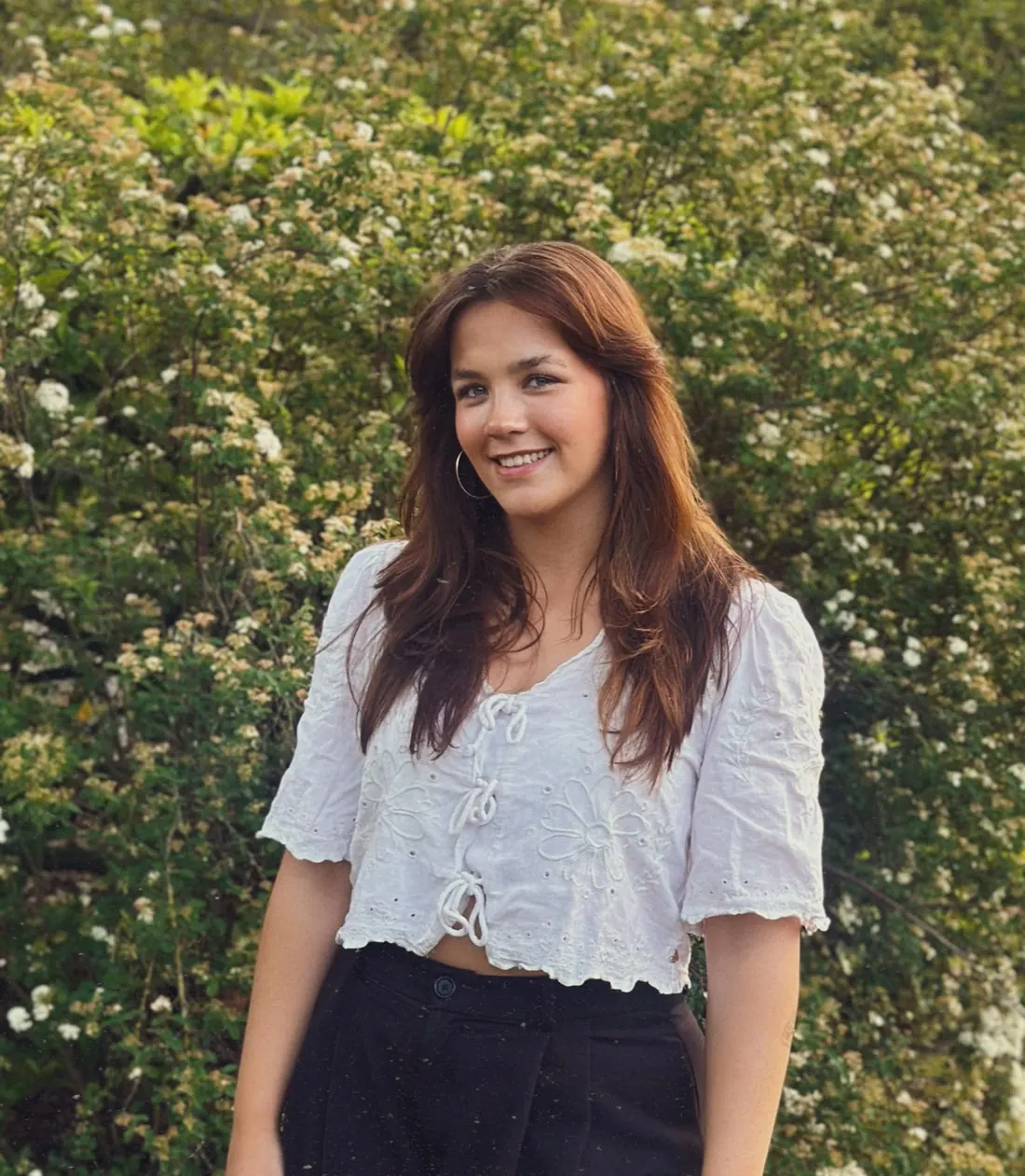 Sanne, masseuse en eigenaresse van Lilies Studio, massagepraktijk voor vrouwen in Lemele (Overijssel), lachend voor een bloeiende struik